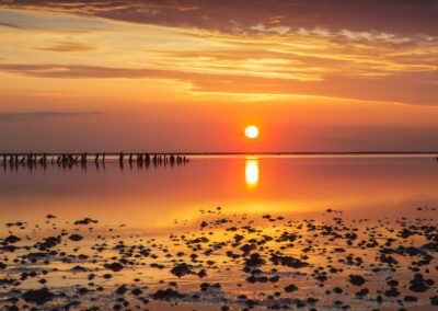 Solnedgang spejlet i det stille vand over den stenede vade